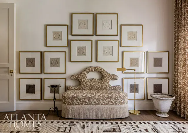 Living room with a patterned bench, gallery wall of framed art, and fringed rug.