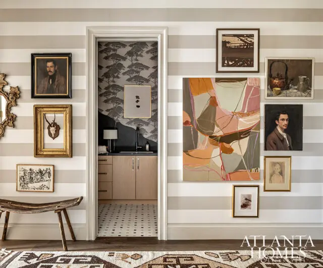 Hallway with striped wallpaper, eclectic art, and a wet bar visible through doorway.