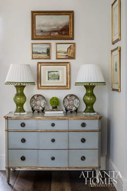 Gray dresser with gold trim, green lamps, and framed art on wall