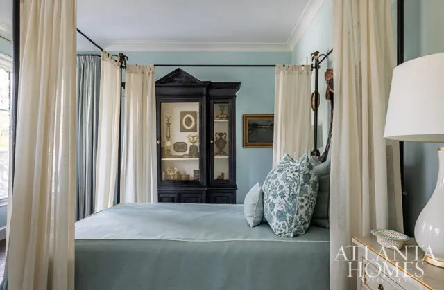 Bedroom with a four-poster bed, light blue walls, and a black curio cabinet filled with decorative