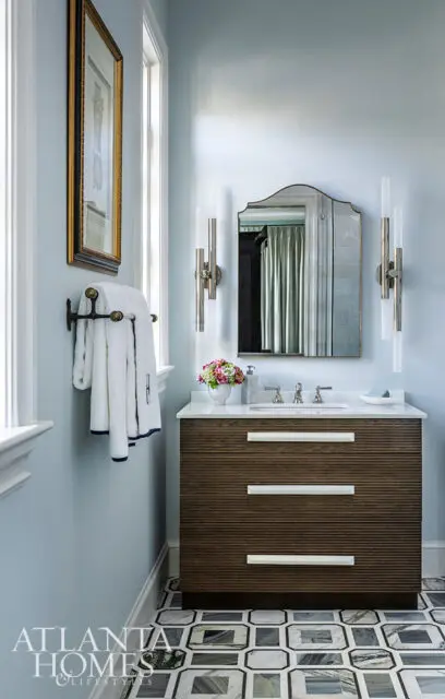 Powder room with light blue walls, wood vanity, marble countertop, and geometric floor tiles.