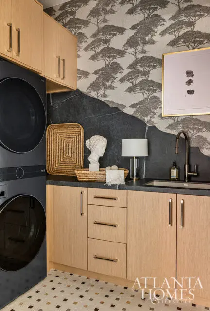 Laundry room with stacked black washer and dryer, light wood cabinets, dark stone backsplash, and