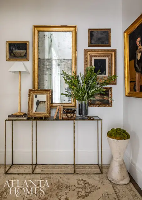 Gold framed mirrors and artwork above a console table with books and greenery