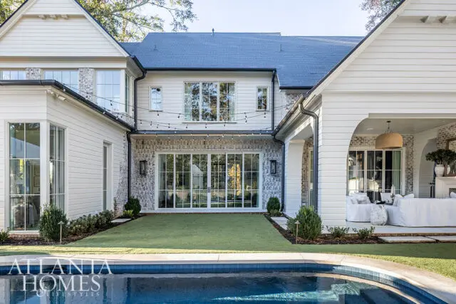 White house with brick accents, large windows, string lights, and a covered patio overlooking a