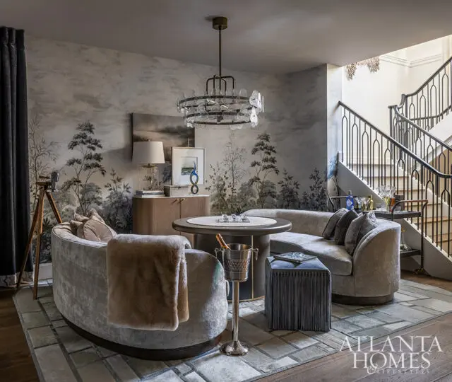 Living room with curved gray sofa, round table, and scenic wallpaper. Atlanta Homes logo visible.