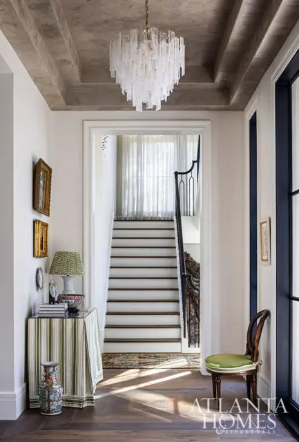 Hallway with a glass chandelier, striped table, and staircase with white steps and dark treads.