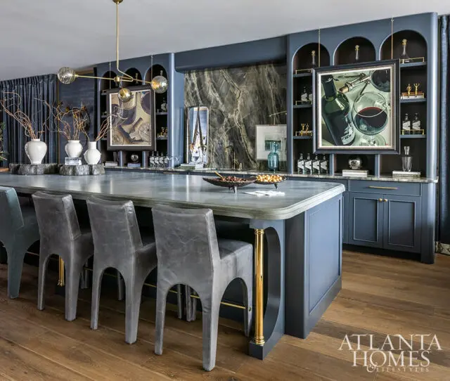 Dark blue kitchen island with gray bar stools, marble countertop, and arched shelving with artwork