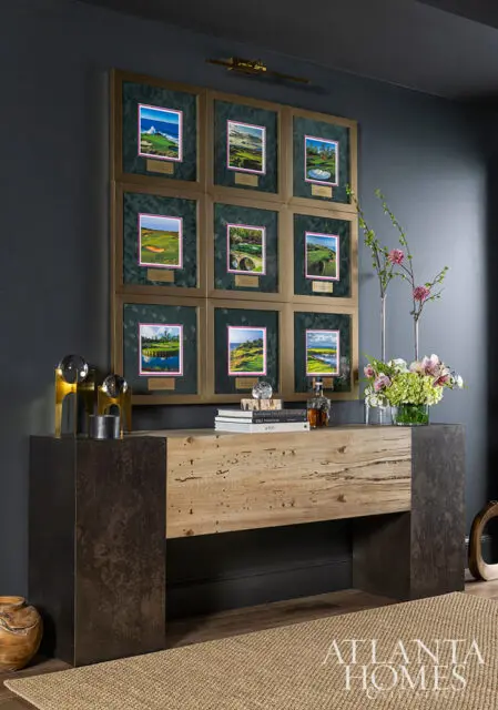 Nine framed golf course photos above a console table with books and flowers