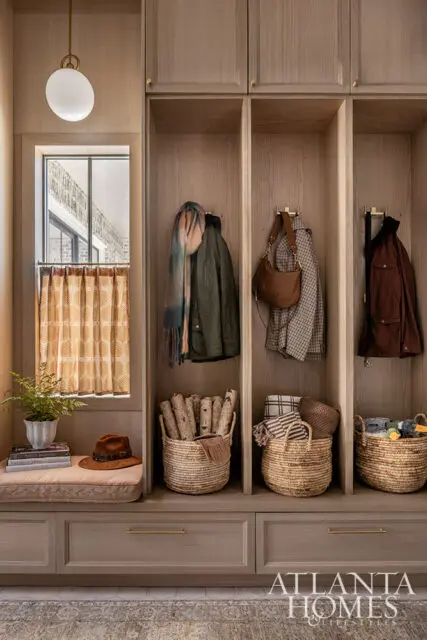 Wood paneled mudroom with built-in cubbies holding coats, bags, and baskets.