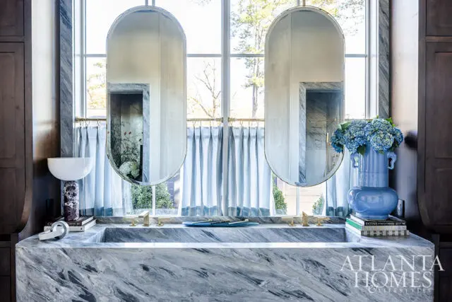 Marble bathroom vanity with double oval mirrors, brass faucets, and blue hydrangeas