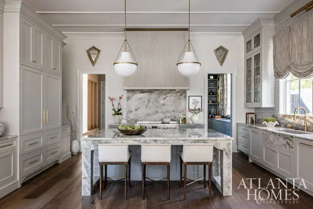 Gray kitchen with marble island, white pendant lights, and brass hardware.