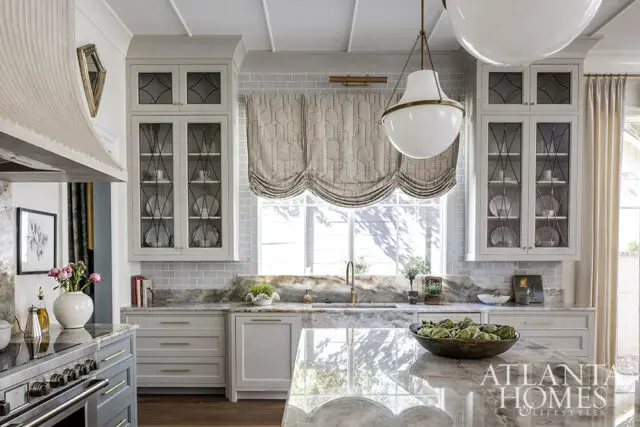 Gray and white kitchen with marble countertops, glass-front cabinets, and a large island.