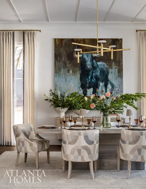 Dining room with abstract bull painting, geometric chairs, and floral arrangements.