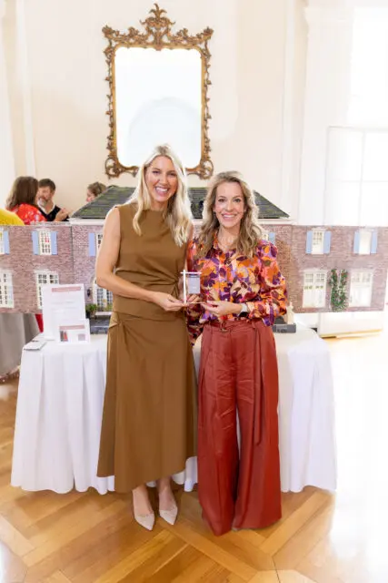 Two women holding awards in front of a dollhouse display