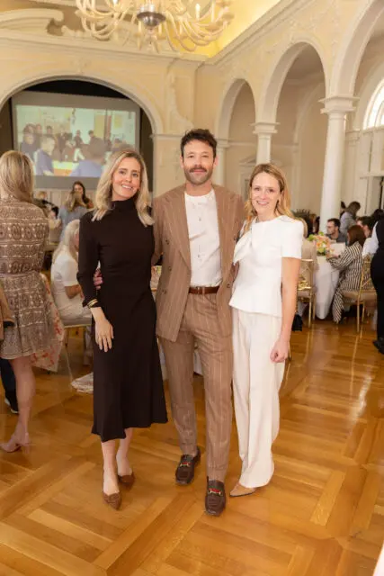 Three people posing in a ballroom with a projector screen behind them.