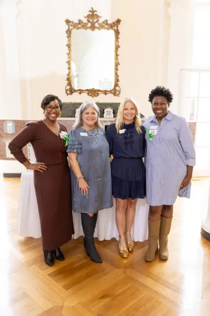 Four women posing for a photo in front of a miniature house model.