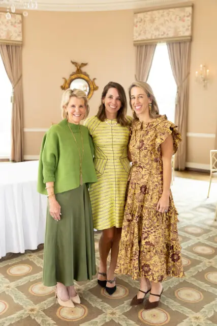 Three women smiling, wearing dresses in green, yellow, and gold floral print.