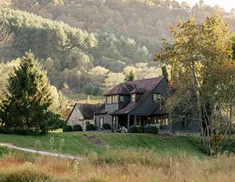 Dark gray house with stone accents nestled in a grassy hillside with trees.