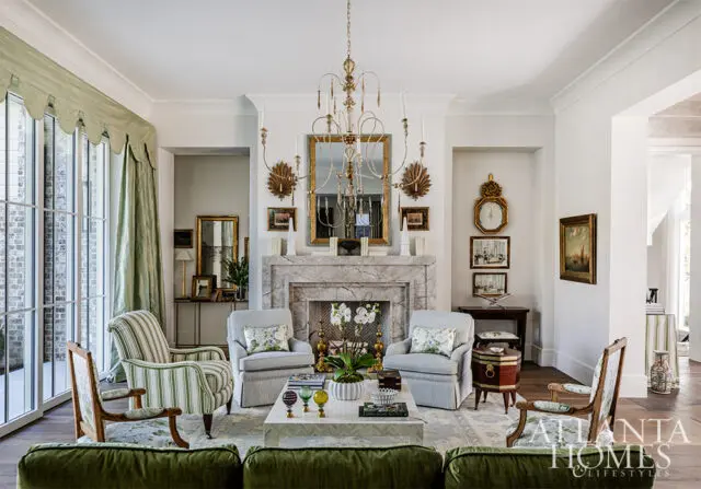 Living room with marble fireplace, ornate chandelier, and green striped armchairs.
