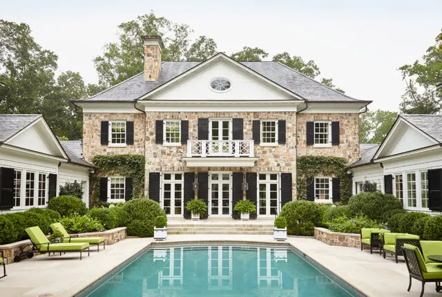 Stone house with black shutters, white trim, and a balcony overlooking a pool