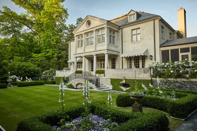 Stone mansion with manicured lawn, formal gardens, and mature trees.