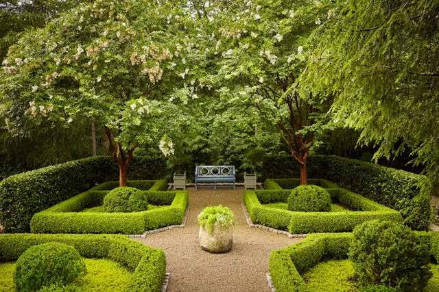 Formal garden with manicured boxwood hedges, gravel paths, and a blue bench.