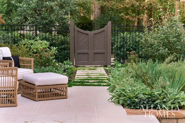 Stone pathway leads through a garden with a dark gate and foliage