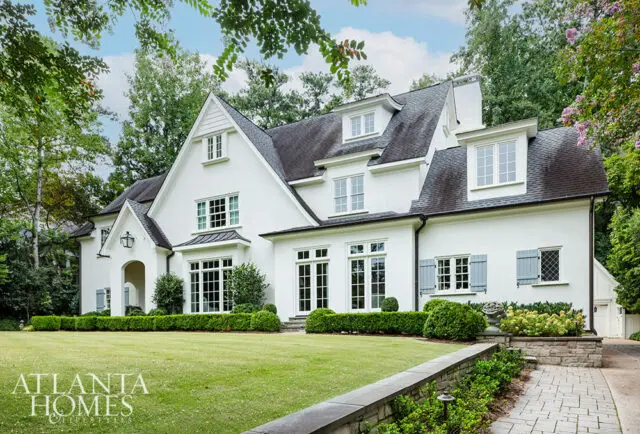 White stucco house with gray shutters, dormer windows, and manicured lawn.