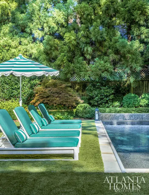 Teal lounge chairs with striped pillows and umbrella beside a pool