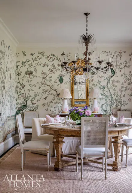 Dining room with chinoiserie wallpaper, round wooden table, and cane-back chairs.