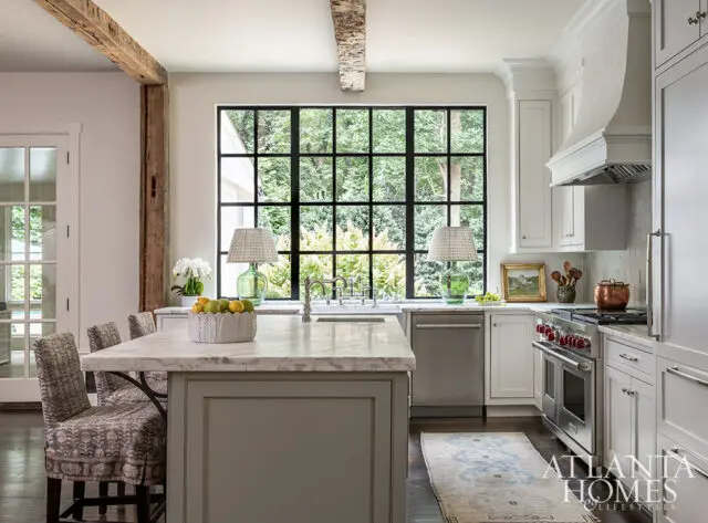 Kitchen with marble island, gray cabinets, white countertops, and large window overlooking trees.