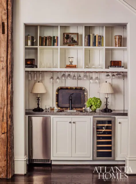 Built-in bar with white cabinetry, stainless steel mini-fridge, wine fridge, and shelves stocked