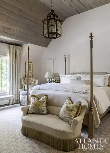 Bedroom with four-poster bed, upholstered bench, and floral pillows. Wood plank ceiling.