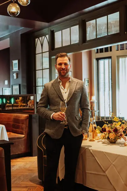 Man in gray tweed jacket holding champagne flute in restaurant