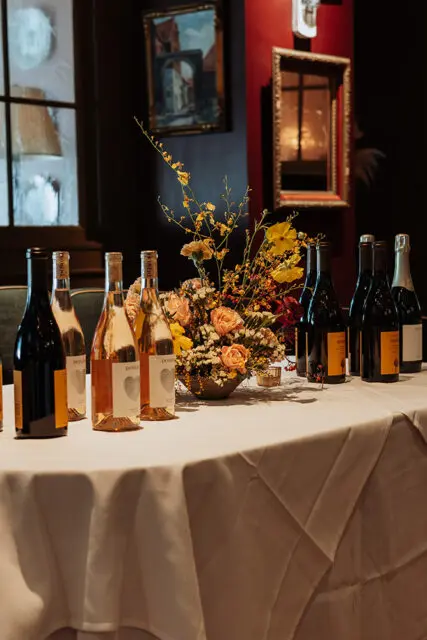 Table with wine bottles and floral arrangement, framed art on wall
