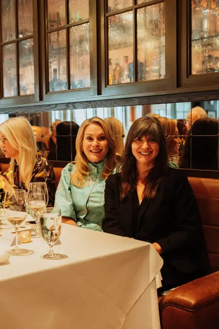 Three women at a table with white tablecloth, leather booth seating, and mirrored wall with