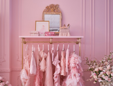 Pink wall with gold accents, clothing rack, and floral arrangement.