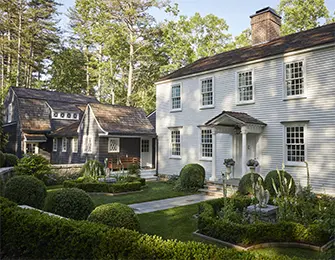 White clapboard house with dark shingled addition and formal gardens