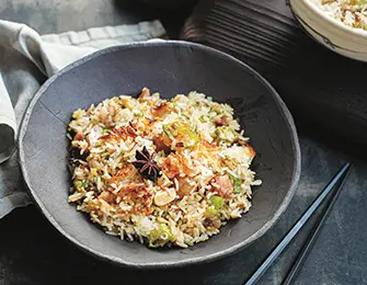 Fried rice with star anise, green onions, and peanuts in a dark gray bowl with chopsticks