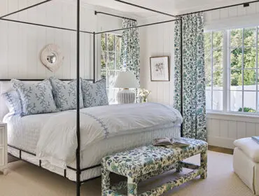 Bedroom with white paneled walls, black canopy bed, blue floral curtains, and upholstered bench.