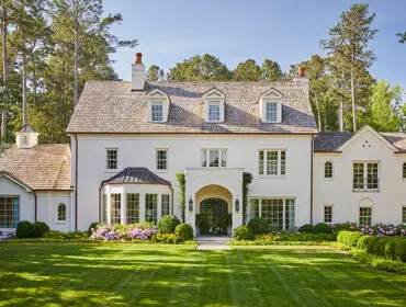 White brick house with wood shingle roof, arched entryway, and manicured lawn.