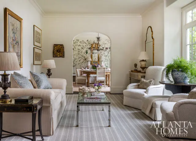 Living room with cream sofa, chairs, and arched doorway to dining room with floral wallpaper.