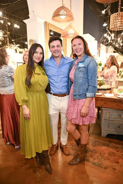Three people posing for a photo in a store with chandeliers and furniture in the background.