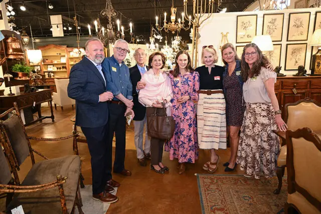 Group of eight people posing in an antique furniture store with chandeliers and ornate furniture in the background.