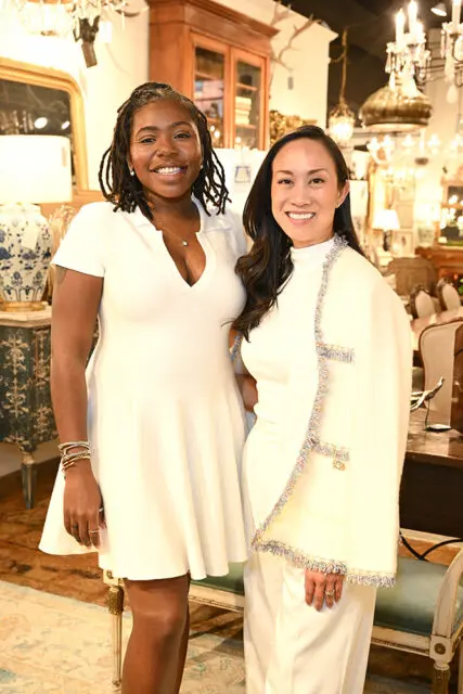 Two women smiling, one in a white dress, the other in a white suit and jacket.