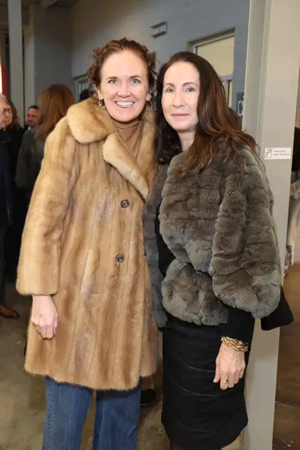 Elizabeth Wilson and Felicia Feaster pose for a photo. Wilson wears a tan fur coat and jeans. Feaster wears a grey fur coat and black skirt.