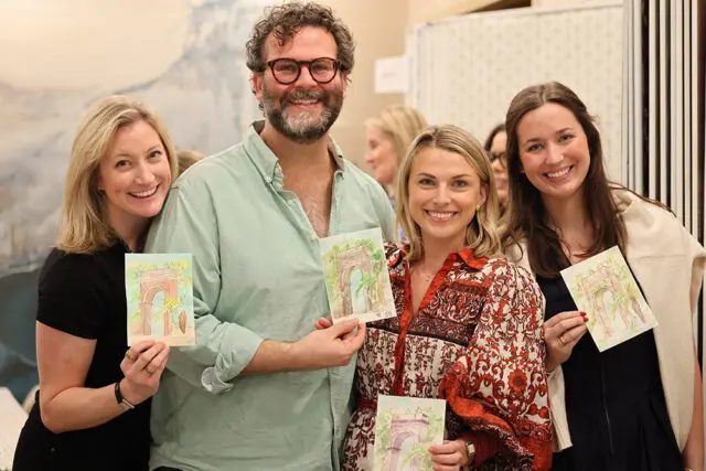 Four people smiling and holding up small watercolor paintings of an arched entryway with greenery.