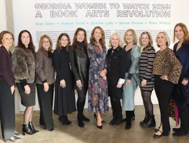Group portrait of ten women standing in front of a wall with text that reads 'GEORGIA WOMEN TO WATCH 2026: A BOOK ARTS REVOLUTION' and names including Eliza Bentz, Hannah Israel, Cynthia Lollis, Serena Perrone, and Eileen Wallace.