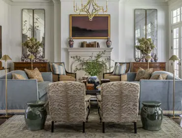 Living room with light blue sofas, animal print accent chairs, ornate fireplace, and tall mirrors flanking a dresser.