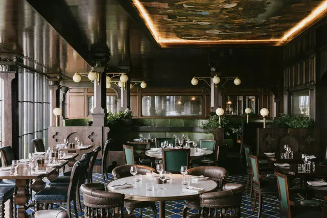 Restaurant dining room with dark wood paneling, green banquettes, and a mural on the ceiling.